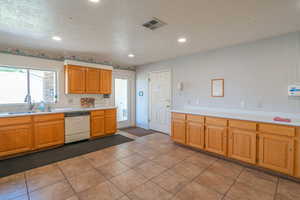 Kitchen with a textured ceiling, light countertops, white dishwasher, recessed lighting, and light tile patterned floors