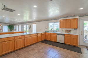 Kitchen with a textured ceiling, light countertops, white dishwasher, recessed lighting, and a peninsula
