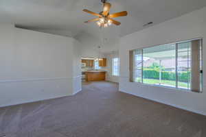 Unfurnished living room with carpet floors, a ceiling fan, a chandelier, and high vaulted ceiling