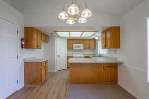 Kitchen featuring light countertops, a peninsula, white appliances, pendant lighting, and brown cabinets