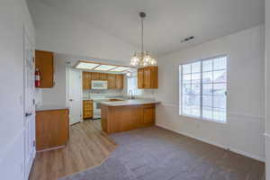Kitchen featuring light countertops, vaulted ceiling, a peninsula, white appliances, and brown cabinetry