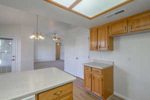 Kitchen with light countertops, pendant lighting, brown cabinets, a chandelier, and light wood-type flooring