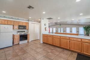 Kitchen featuring white appliances, light countertops, recessed lighting, a textured ceiling, and light tile patterned flooring