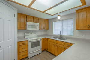 Kitchen featuring white appliances, light countertops, light wood-type flooring, and brown cabinets