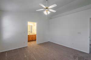 Unfurnished bedroom featuring dark carpet, vaulted ceiling, ensuite bath, and ceiling fan