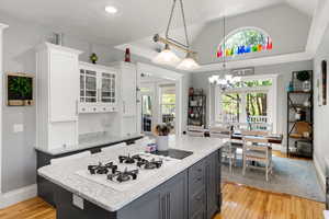 Kitchen featuring light wood-type flooring, decorative light fixtures, light stone counters, and high vaulted ceiling