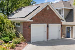 View of front of property featuring a shingled roof, concrete driveway, a garage, solar panels, and brick siding