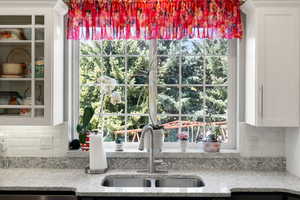Kitchen featuring tasteful backsplash, light stone countertops, white cabinetry, and glass insert cabinets