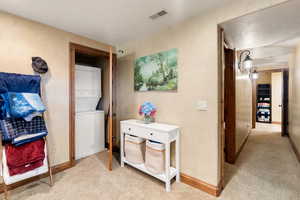 Hallway with light colored carpet, estacked washer and dryer, a textured ceiling, and a textured wall