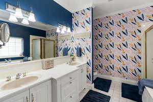 Bathroom with wallpapered walls, a stall shower, ornamental molding, double vanity, and light tile patterned flooring