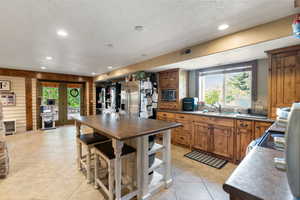 Kitchen with brown cabinets, a textured ceiling, light tile patterned floors, recessed lighting, and appliances with stainless steel finishes