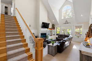Living area with a fireplace, healthy amount of natural light, high vaulted ceiling, stairway, and light carpet