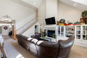 Carpeted living area featuring high vaulted ceiling, a glass covered fireplace, and stairs