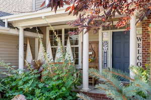Doorway to property featuring covered porch, brick siding, and roof with shingles