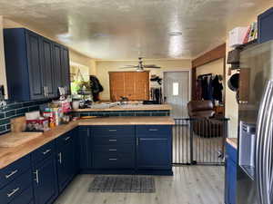 Kitchen featuring blue cabinets, stainless steel fridge with ice dispenser, a peninsula, light wood-style flooring, and a textured ceiling