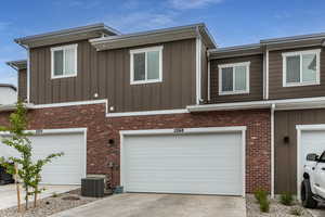 View of property exterior featuring an attached garage, concrete driveway, board and batten siding, and brick siding