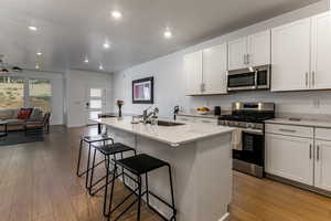 Kitchen with appliances with stainless steel finishes, a center island with sink, light wood finished floors, light stone counters, and white cabinets