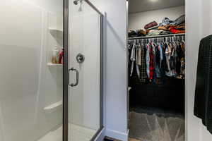Bathroom with a textured ceiling, a spacious closet, and a shower stall