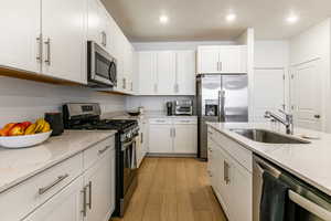 Kitchen with appliances with stainless steel finishes, light stone counters, white cabinetry, light wood finished floors, and recessed lighting