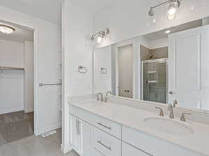 Full bath with a walk in closet, double vanity, a shower stall, light colored carpet, and light tile patterned floors