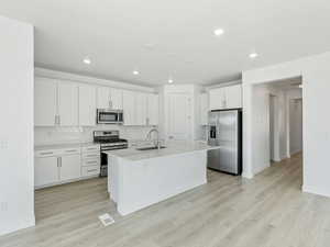 Kitchen with stainless steel appliances, white cabinets, a center island with sink, light wood-style flooring, and recessed lighting
