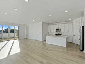 Kitchen featuring open floor plan, a center island with sink, white cabinets, light wood-style floors, and appliances with stainless steel finishes