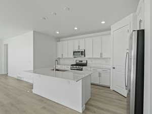 Kitchen featuring stainless steel appliances, white cabinets, a center island with sink, light wood-style flooring, and recessed lighting