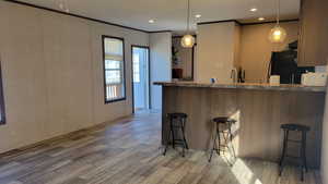 Kitchen featuring hanging light fixtures, a breakfast bar, a peninsula, dark wood-style vinyl flooring, and crown molding