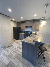 Kitchen featuring a kitchen bar, black appliances, light wood-type flooring, a peninsula, and recessed lighting
