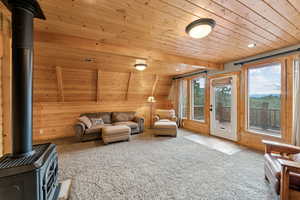 Living area featuring a wood stove, wood ceiling, carpet, and wood walls
