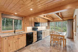 Kitchen featuring plenty of natural light, black appliances, a wooden ceiling with exposed beams, light brown cabinets, and light stone countertops