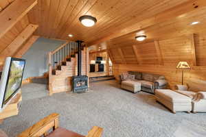 Living room featuring stairs, a wood stove, lofted ceiling, carpet flooring, and wood ceiling