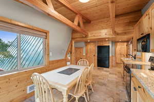 Dining space featuring wood walls, wainscoting, a wooden ceiling with exposed beams, and light stone finish floors