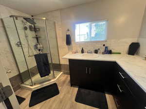 Bathroom with vanity, a marble finish shower, light wood-style floors, and decorative backsplash