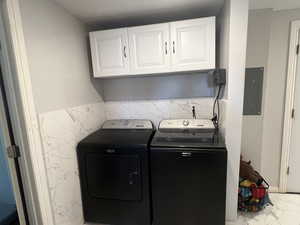 Laundry area featuring marble look tiles, cabinet space, electric panel, and independent washer and dryer