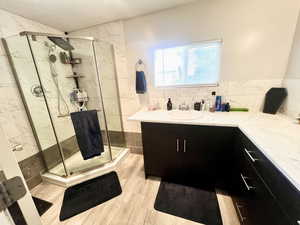 Full bathroom with vanity, a marble finish shower, light wood-style flooring, and backsplash