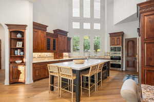 Kitchen featuring tasteful backsplash, a kitchen breakfast bar, a center island with sink, light stone countertops, and a high ceiling