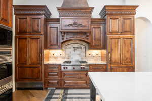 Kitchen featuring backsplash, built in appliances, light stone counters, arched walkways, and light wood-style floors