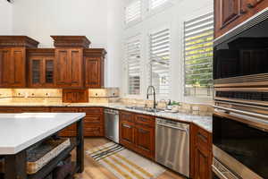 Kitchen featuring stainless steel appliances, glass insert cabinets, light wood-style floors, light stone counters, and decorative backsplash