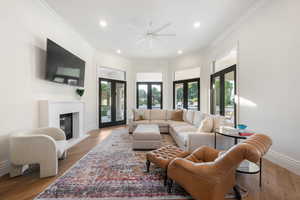 Living room with ornamental molding, light wood-style flooring, recessed lighting, a glass covered fireplace, and french doors