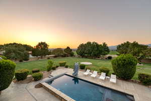 Pool at dusk featuring a water slide, a patio, and a lawn