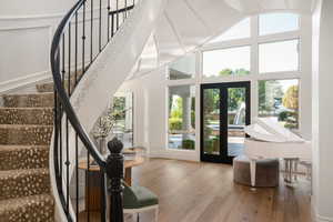 Doorway to outside with hardwood / wood-style floors, high vaulted ceiling, and stairway