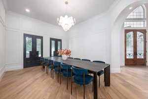 Dining area featuring french doors, a decorative wall, light wood-type flooring, arched walkways, and a chandelier