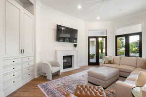 Living room featuring wood finished floors, recessed lighting, crown molding, a glass covered fireplace, and ceiling fan