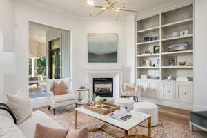 Living room featuring a chandelier, wood finished floors, ornamental molding, a glass covered fireplace, and built in shelves