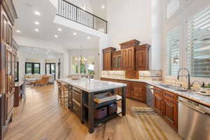 Kitchen with light stone counters, stainless steel dishwasher, light wood-type flooring, tasteful backsplash, and a high ceiling