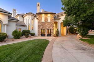 Mediterranean / spanish-style house with stone siding, stucco siding, concrete driveway, a front lawn, and a chimney