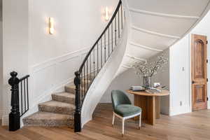 Stairway featuring wood finished floors, a decorative wall, and wainscoting