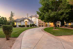 View of front of home with a yard, stucco siding, curved driveway, and stone siding