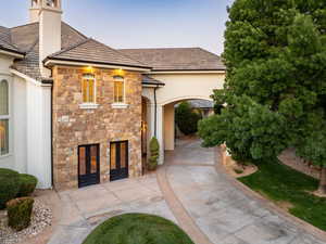 View of front of property with stone siding, stucco siding, concrete driveway, and a chimney